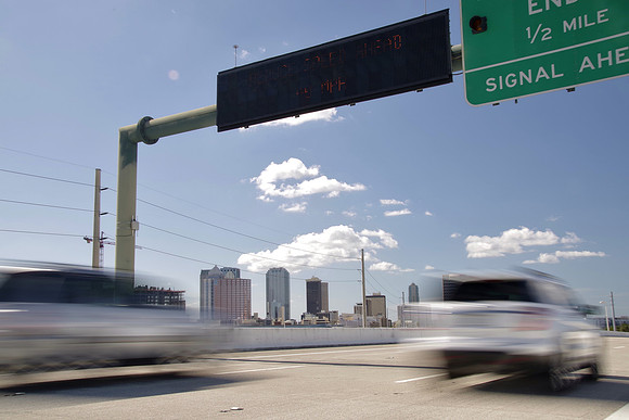 Cars speed under a DMS and by a roadside unit, which communicates with on-board units in the cars.