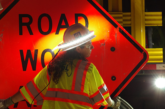 A construction worker wears a halo light on her hard hat as she prepares signs for placement on I-4.